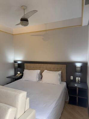A neatly arranged hotel room with a large bed, a bedside table with a lamp, a nightstand with a phone, and a ceiling fan. - Get a Flat 703 Bienal-Ibirapuera (São Paulo)