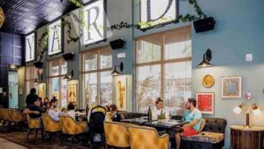 Un restaurante con una barra larga, sillas amarillas y una pared azul con la palabra 'YARD' a la vista.