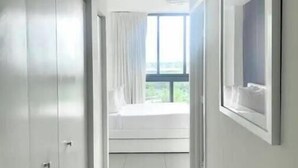 Un pasillo estrecho y bien iluminado con un ventanal grande al final, que da a una habitación con cama y cortinas.