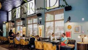 En restaurant med gule stole, borde og en blå væg med et stort skilt, der står 'YARD'.