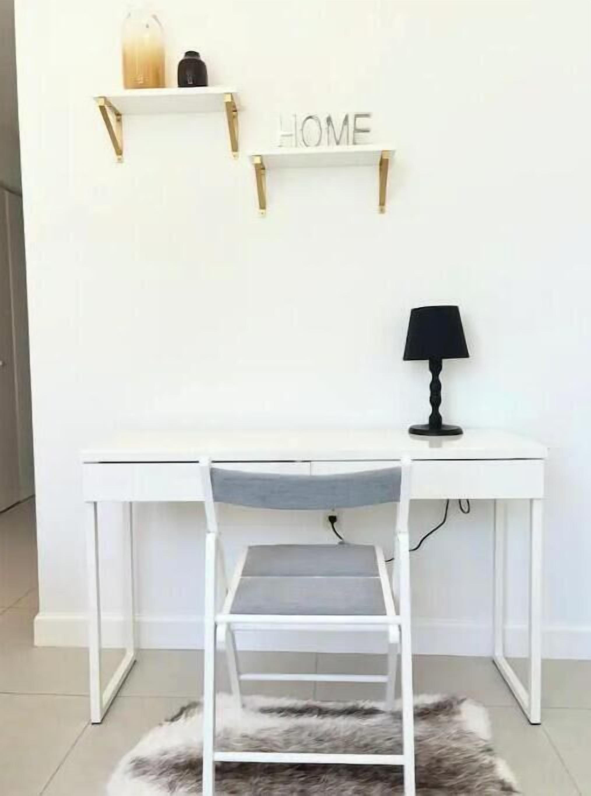 Un escritorio blanco con una silla, una lámpara y un cartel en la pared que dice 'HOME'.