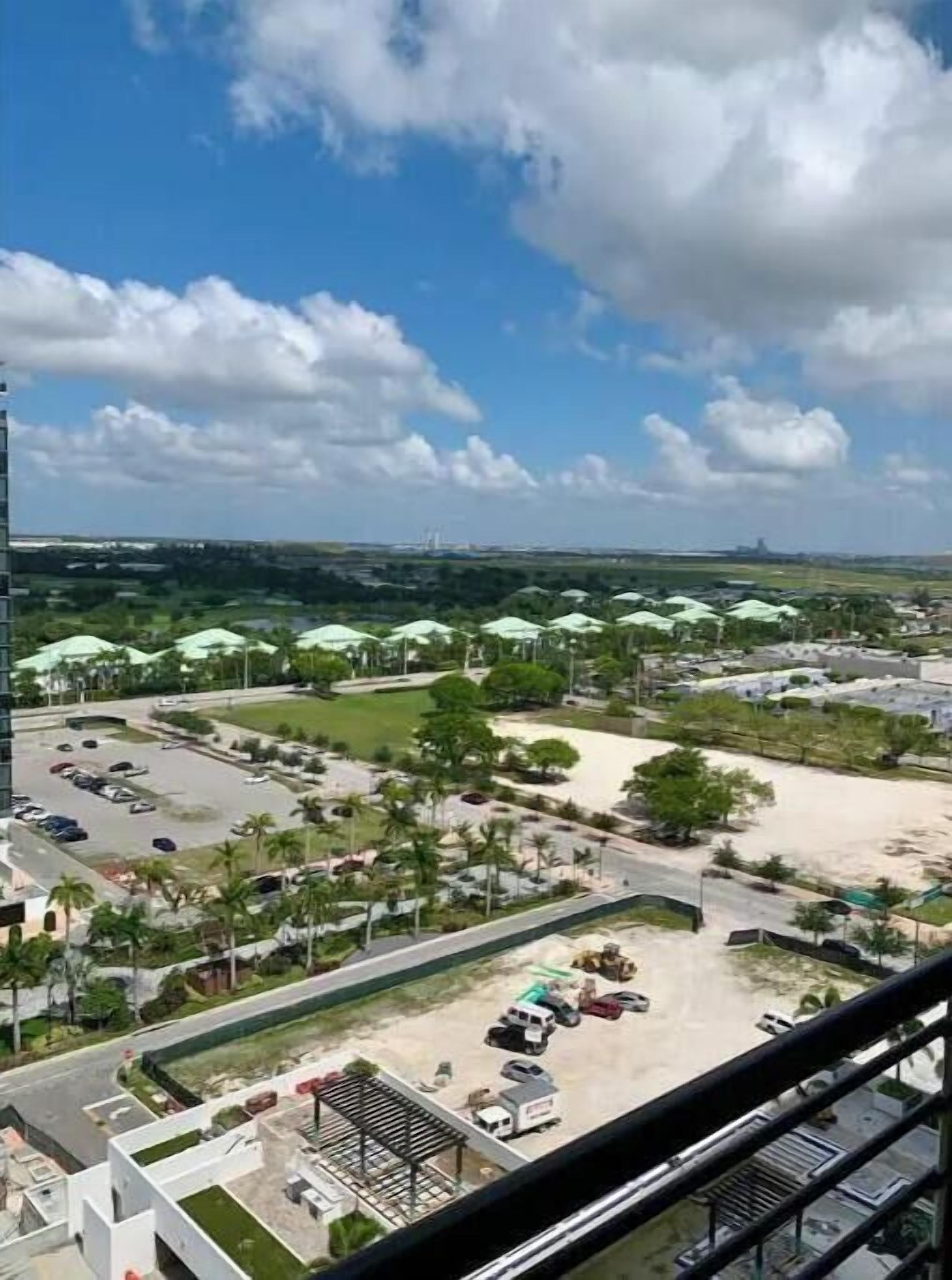 A view of a parking lot with several cars, a building with a green roof, and a clear sky with clouds.