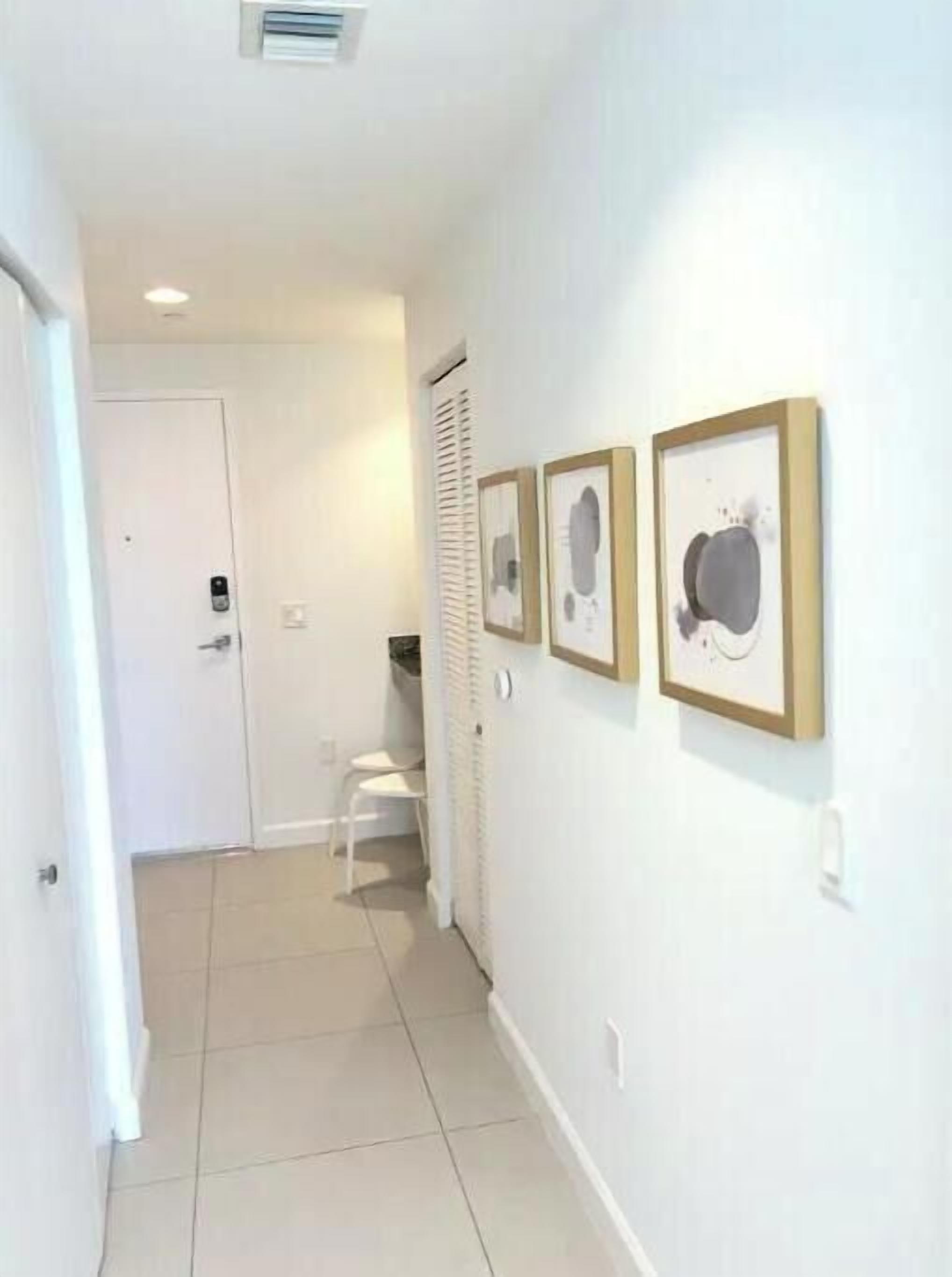 A hallway with a white door, a white chair, and three framed pictures on the wall.
