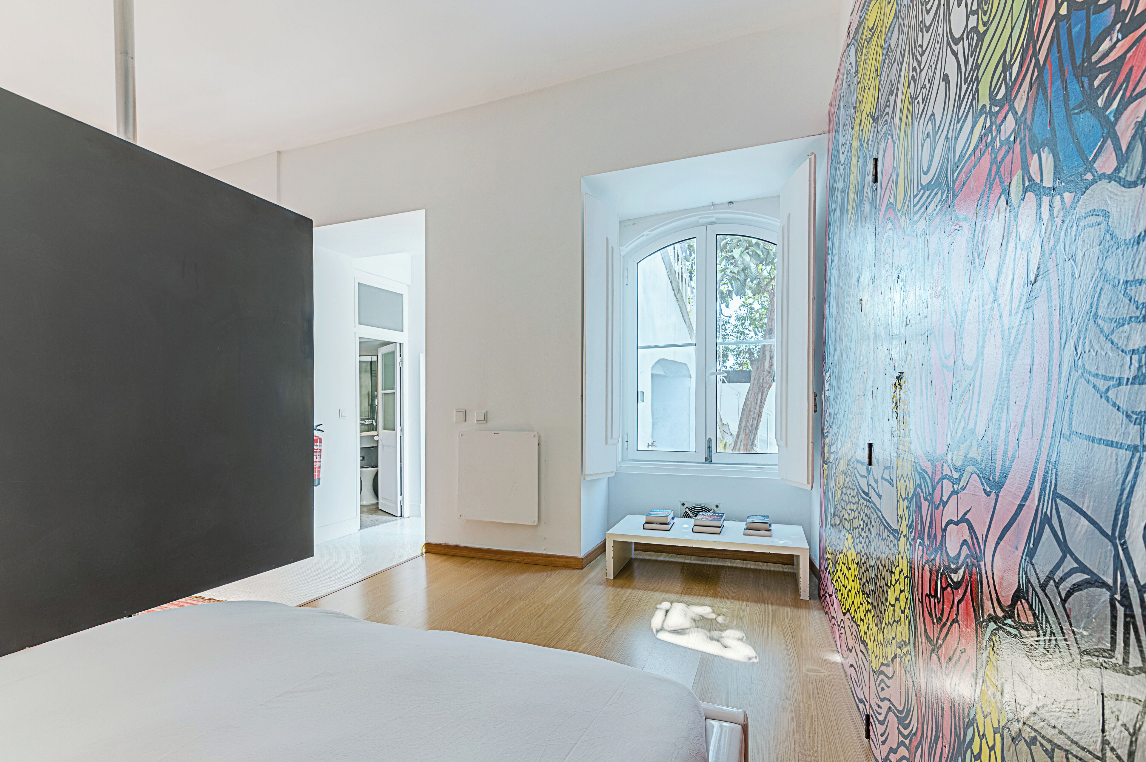 A modern room with a large window, a white bench, and a colorful abstract mural.