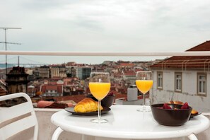A table with breakfast items and glasses of orange juice on a balcony overlooking a cityscape. - Portas do Castelo Apartments (Lisbon)