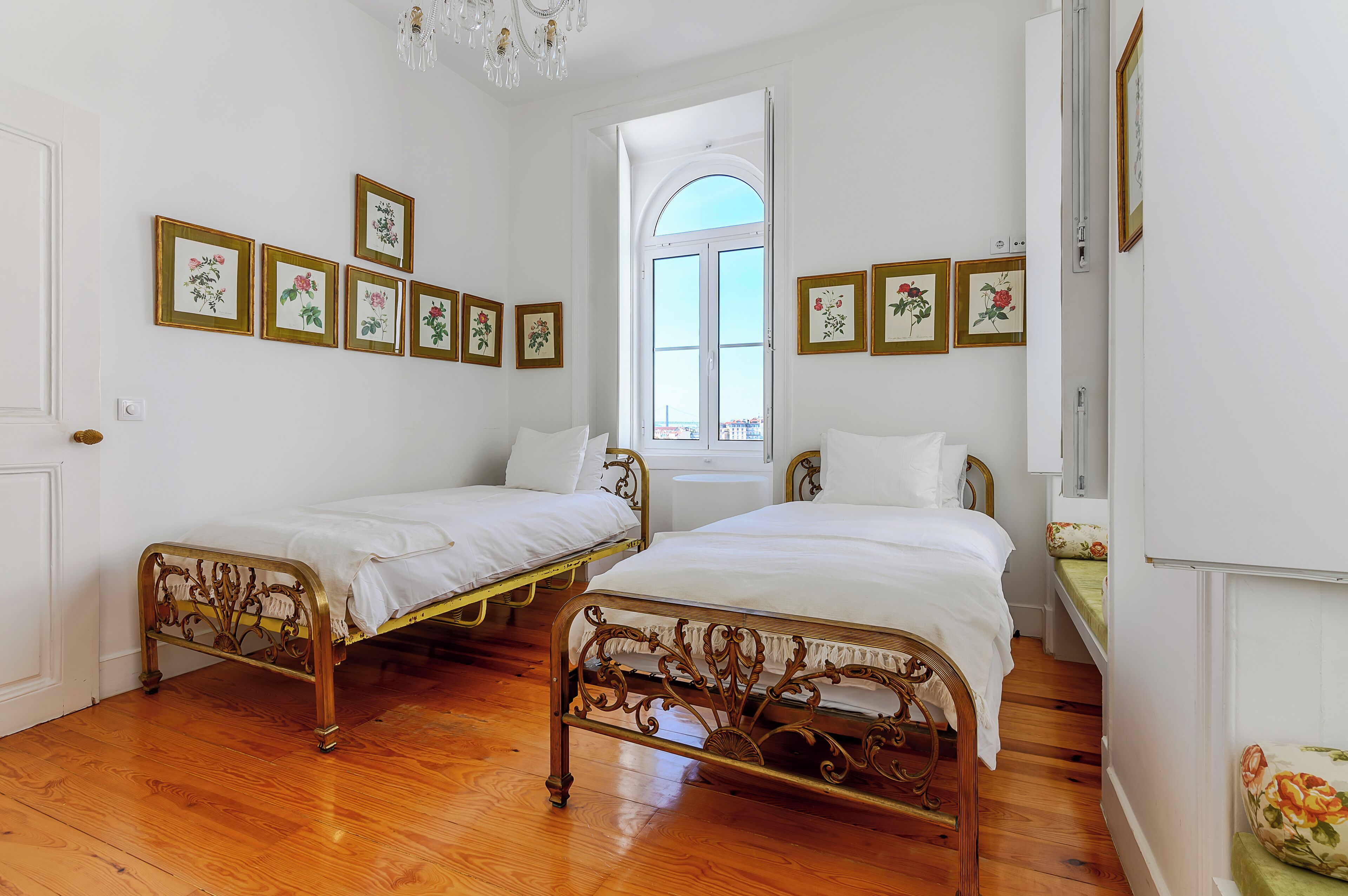 A room with two beds, wooden flooring, and floral wall art.