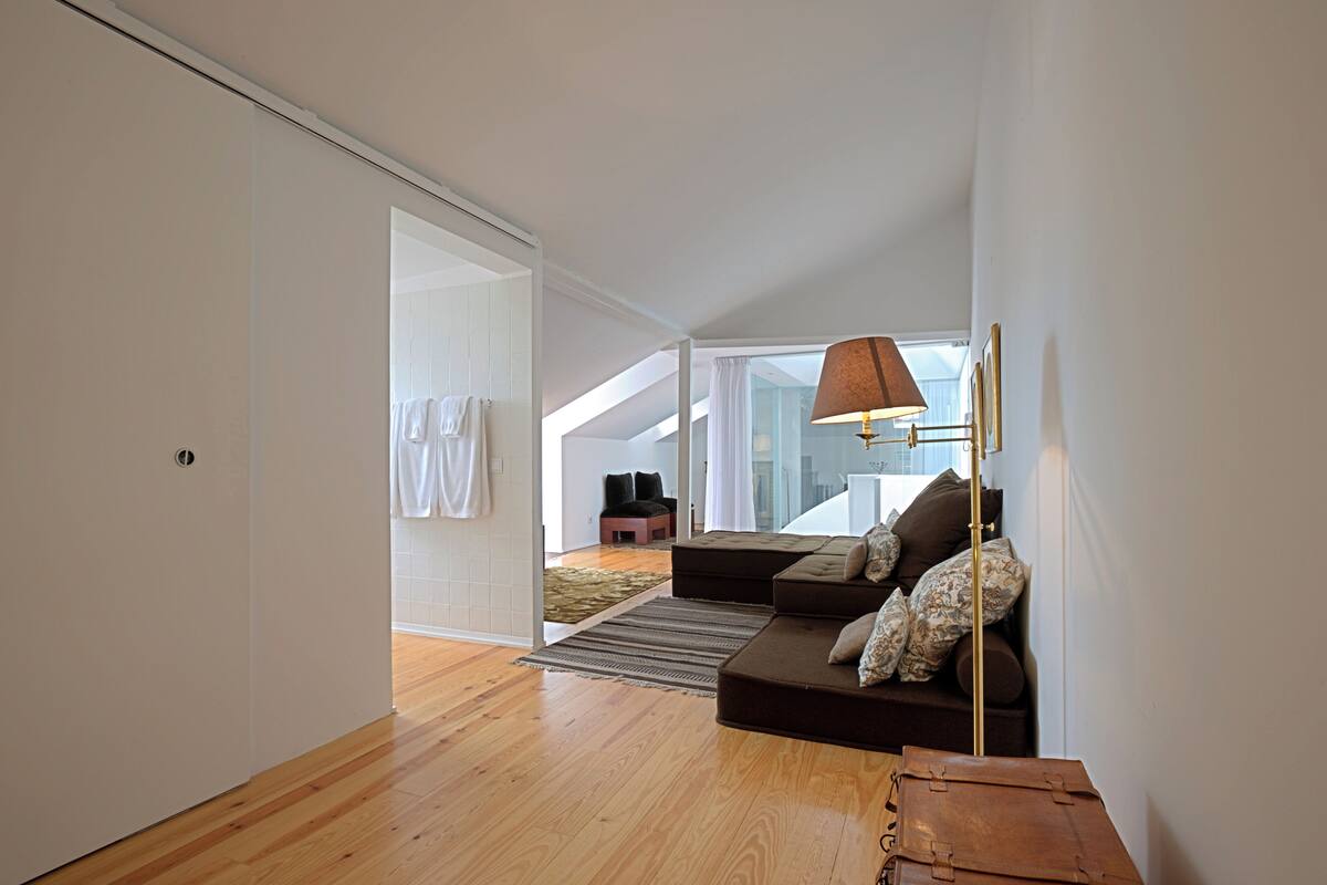 A modern living room with a sofa, a lamp, and a view of the city through large windows.