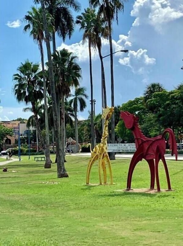 A park with two animal sculptures, one yellow and one red, surrounded by palm trees and a clear sky. - Cozy 1/1 Apartment in the heart of Coconut Grove (Miami)