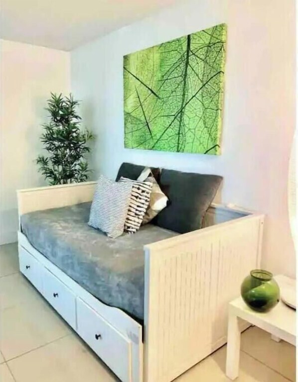 A small, modern bedroom with a bed, a nightstand, a green vase, and a wall-mounted abstract painting. - Cozy 1/1 Apartment in the heart of Coconut Grove (Miami)
