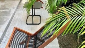 Un pasillo con una silla de madera, plantas en macetas y una silla de metal.