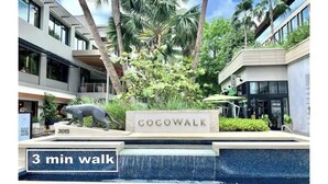 Señal de 'Cocowalk' con el rótulo '3 minutos a pie', rodeada por una fuente y palmeras.