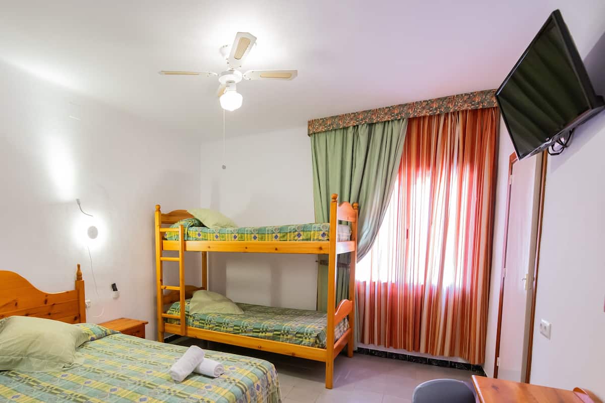 A room with bunk beds, a ceiling fan, a television, and curtains.