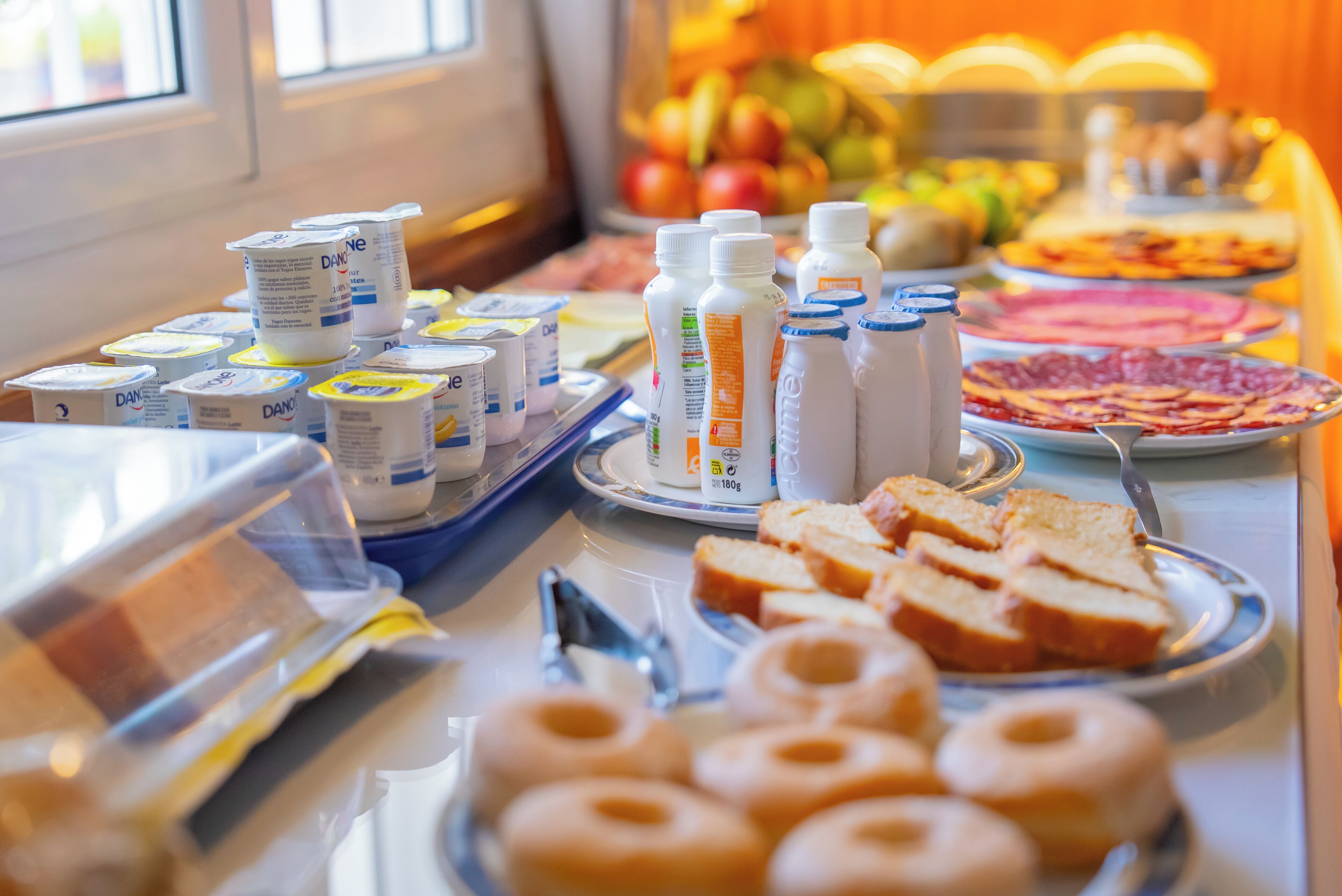 A buffet with various food items including yogurt, milk, bread, and donuts.