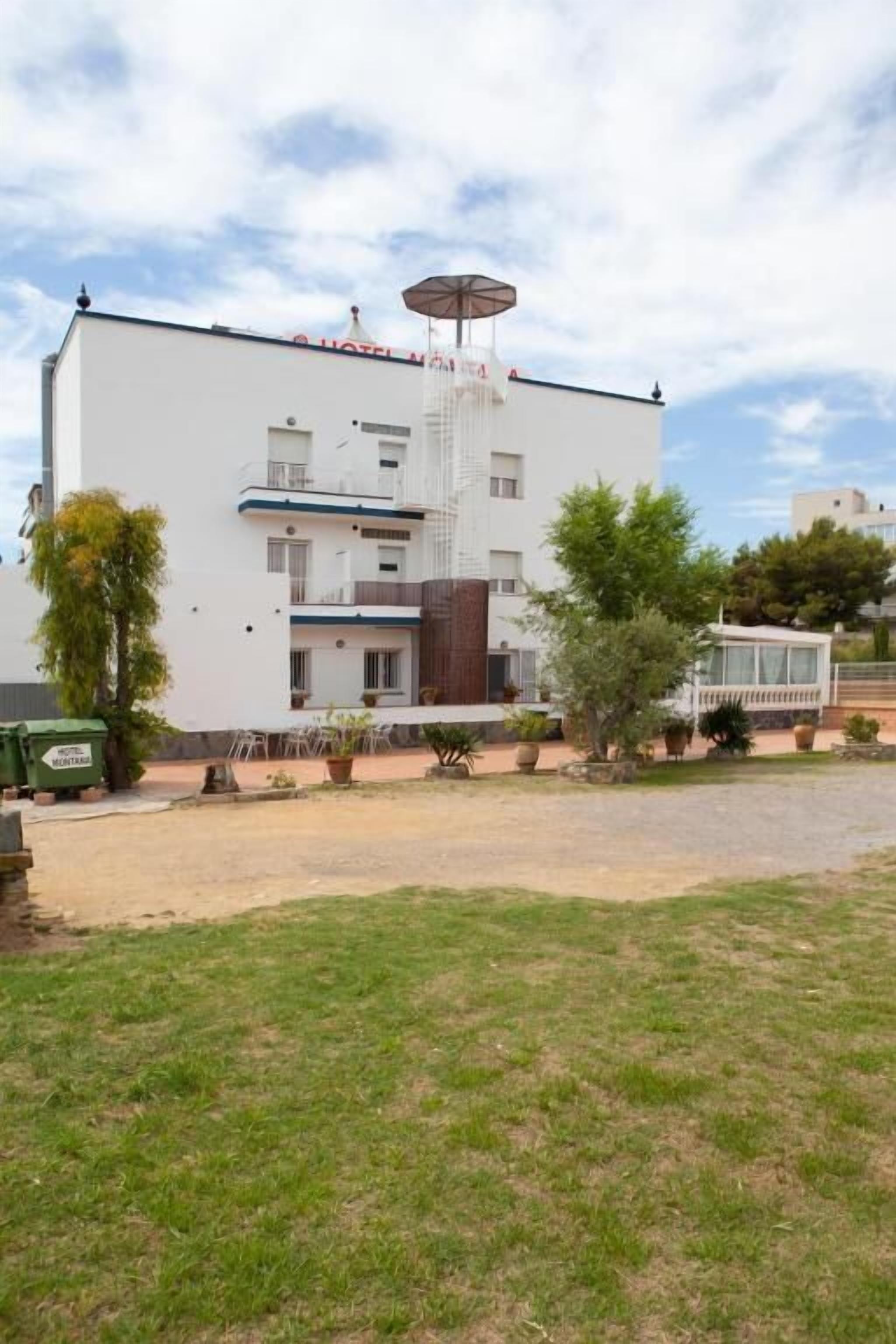 A modern hotel with a flat roof, a covered outdoor area, and a well-maintained lawn.
