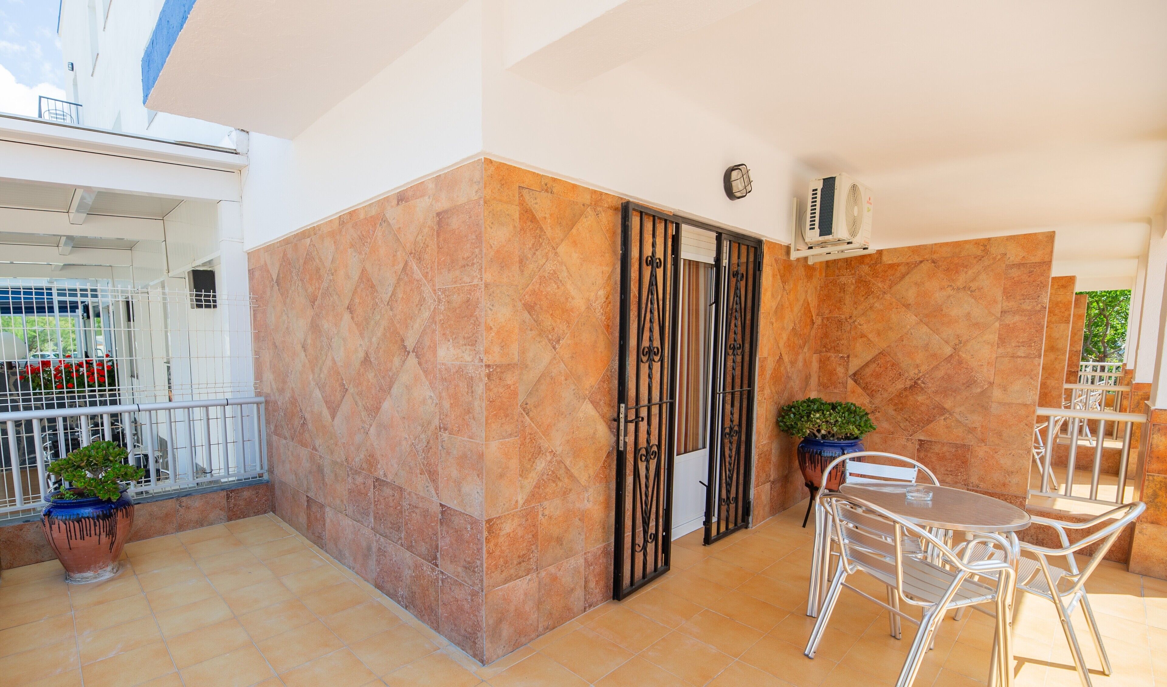 A balcony with a tiled floor, a metal gate, a potted plant, and a table with chairs.