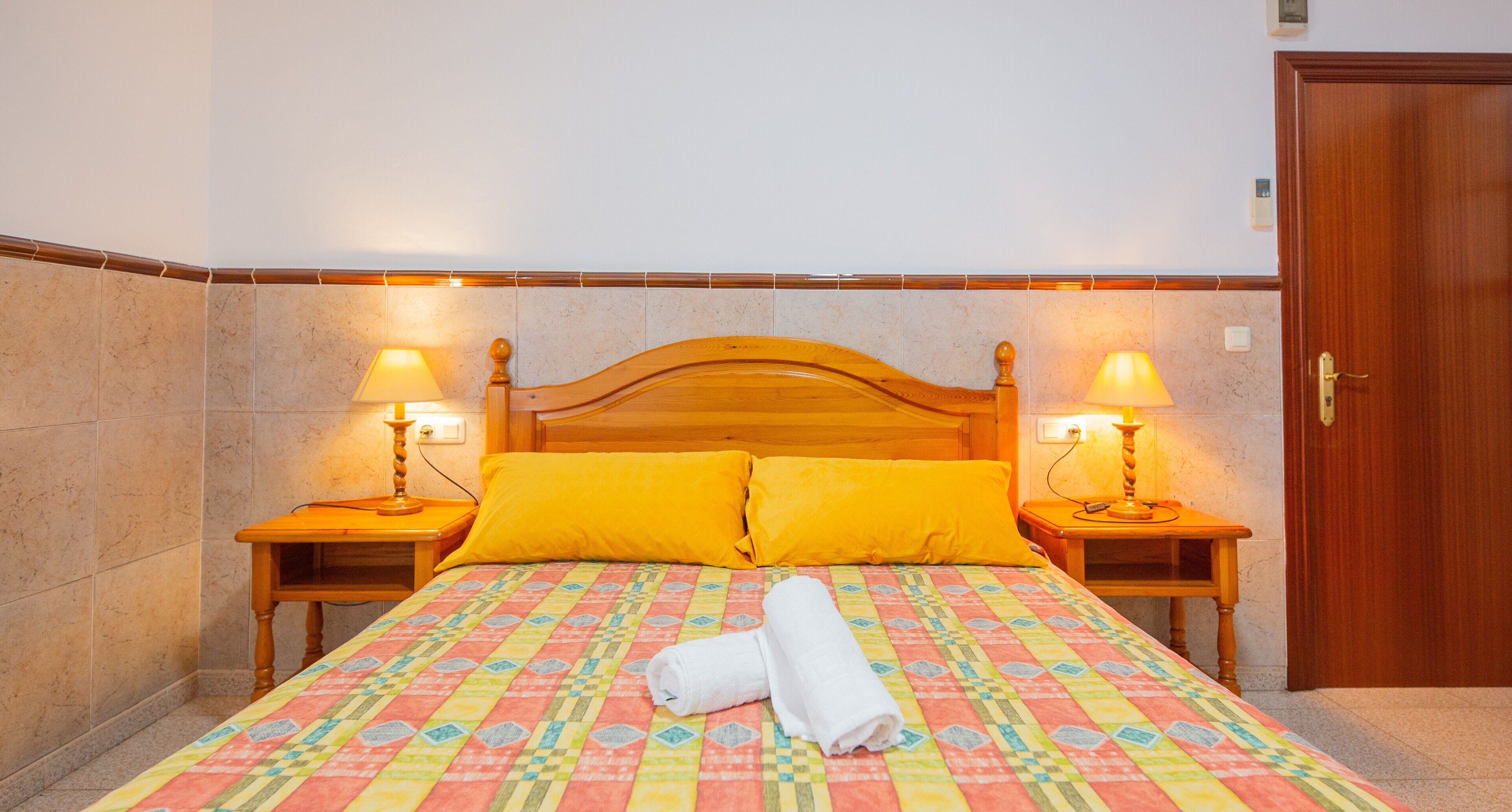 A hotel room with a wooden bed, two bedside lamps, and a door.