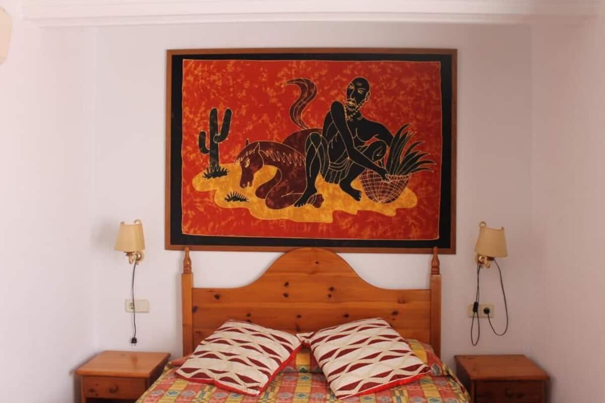 A bedroom with a wooden bed, two bedside tables, and a framed artwork above the bed.