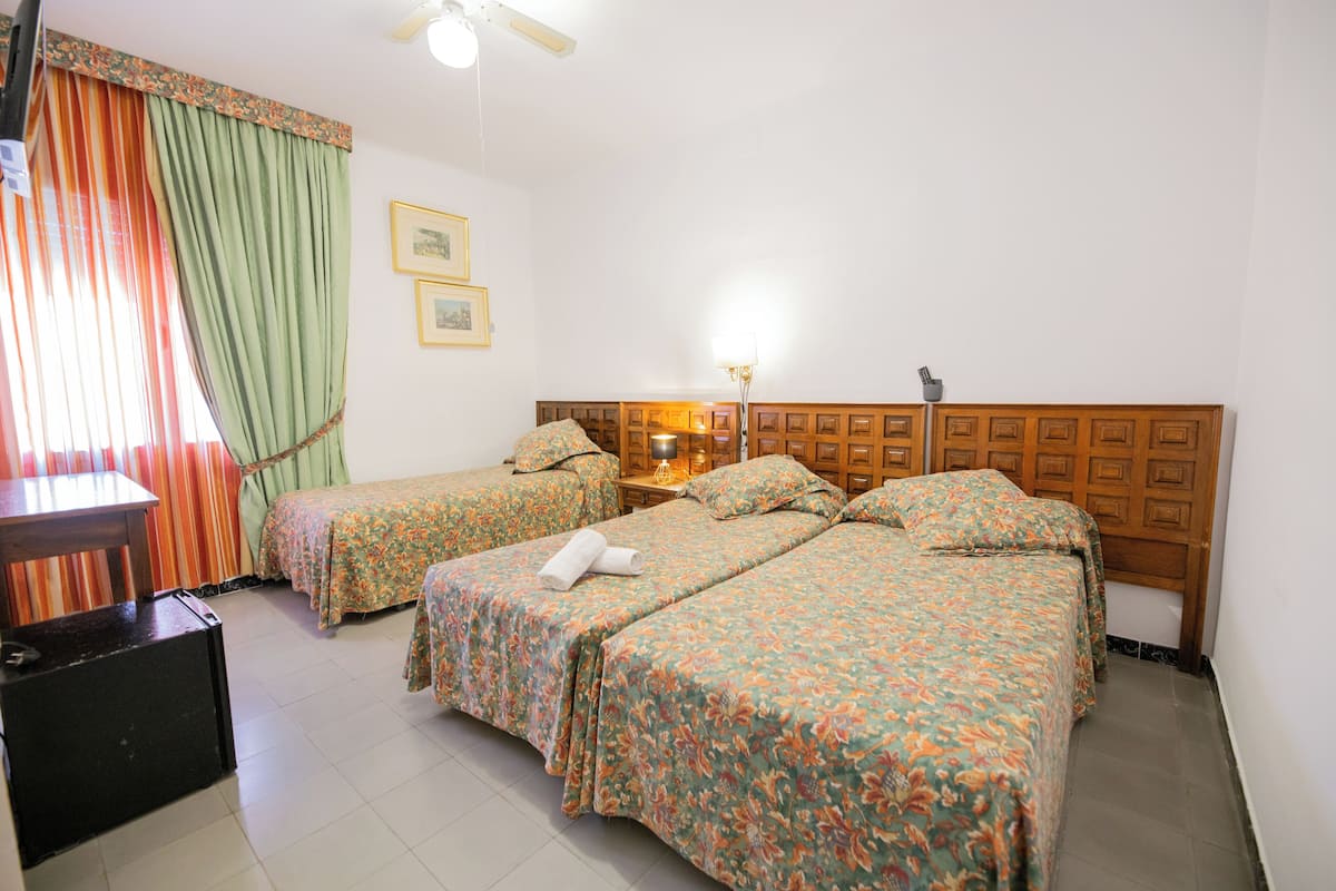 A hotel room with two single beds, a wooden headboard, a desk with a chair, a lamp, and a suitcase.