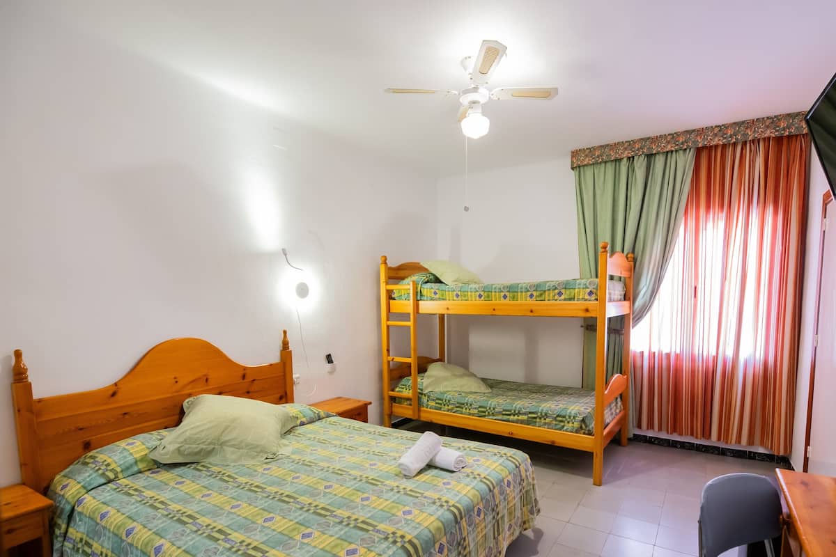 A room with two bunk beds, a desk, a chair, a ceiling fan, and a window with curtains.