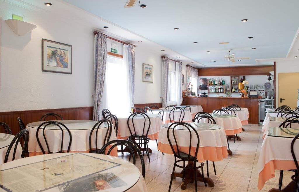 Un restaurant avec des tables rondes, des chaises noires et un bar situé au fond de la salle.