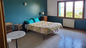 Une chambre à coucher comprenant un lit, une petite table, une table de chevet, une fenêtre avec vue et un ventilateur de plafond.