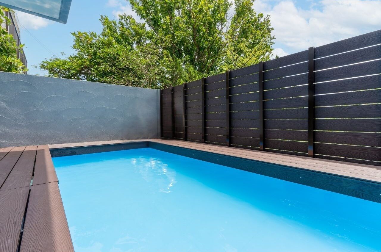 A swimming pool with a wooden deck and a dark fence.