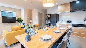 A modern kitchen with a flat-screen TV, wooden cabinets, and a dining area with a wooden table set for six. - Grandioso Okinawa Pool Villa Onna 13 (Onna)