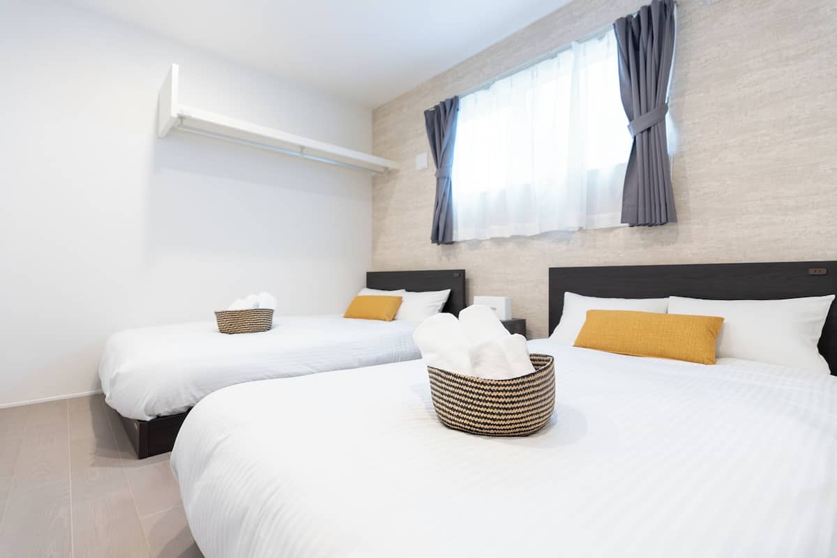 A hotel room with two beds, a large window with curtains, a wall-mounted shelf, and a basket on the bed.