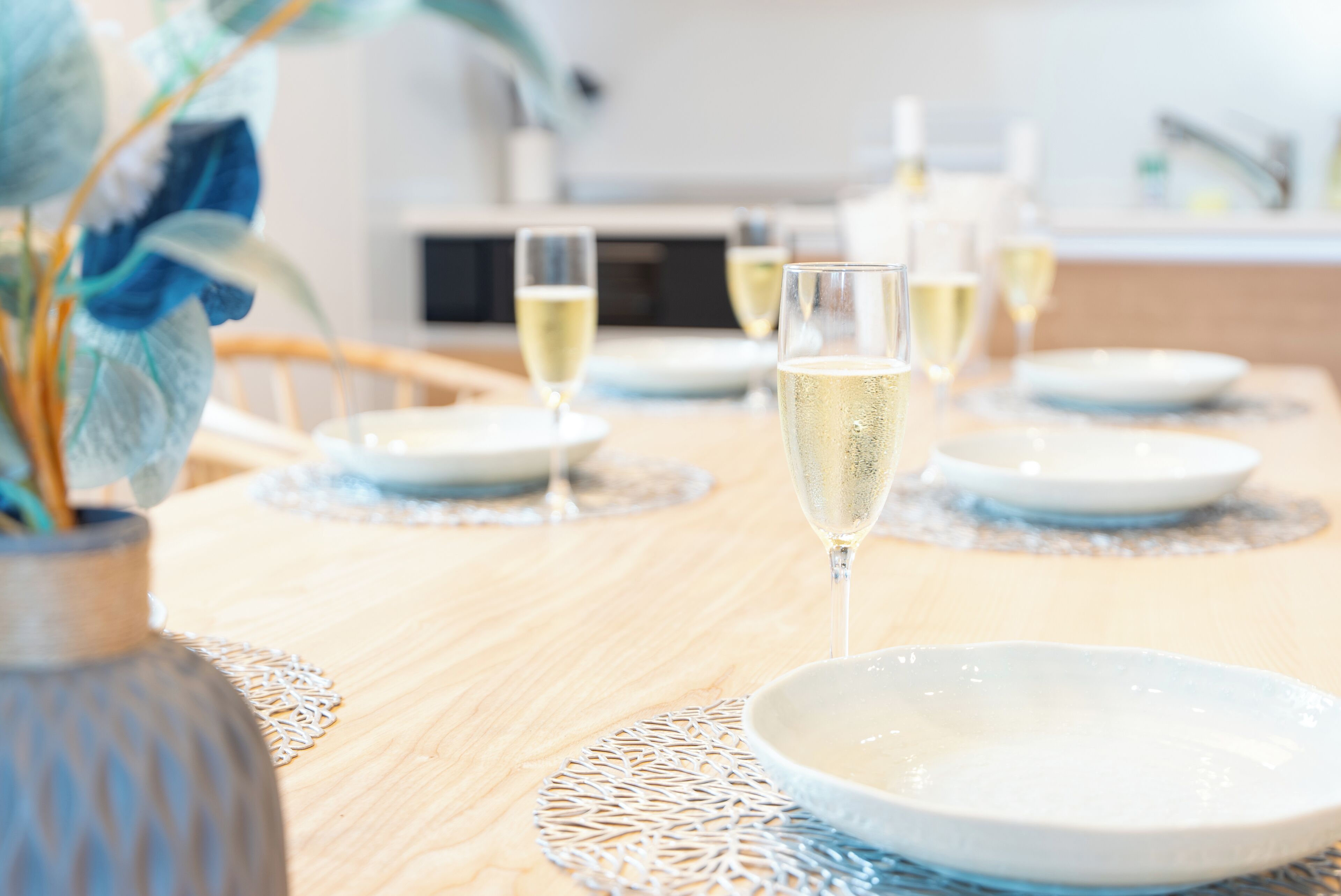 A dining table with a vase of flowers, clear glassware, and white plates.