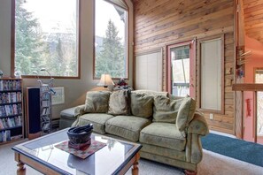 A cozy living room with a sofa, a coffee table, a bookshelf, and large windows.