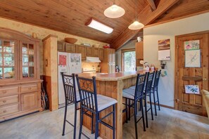 A rustic kitchen with wooden cabinets, a central island with bar stools, and a wooden ceiling.