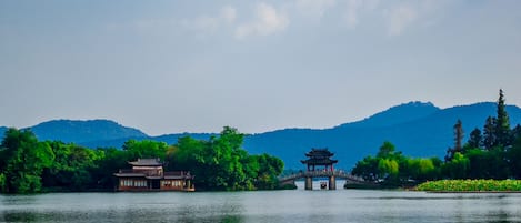 A traditional Chinese pavilion over a lake, surrounded by lush greenery and mountains in the background.