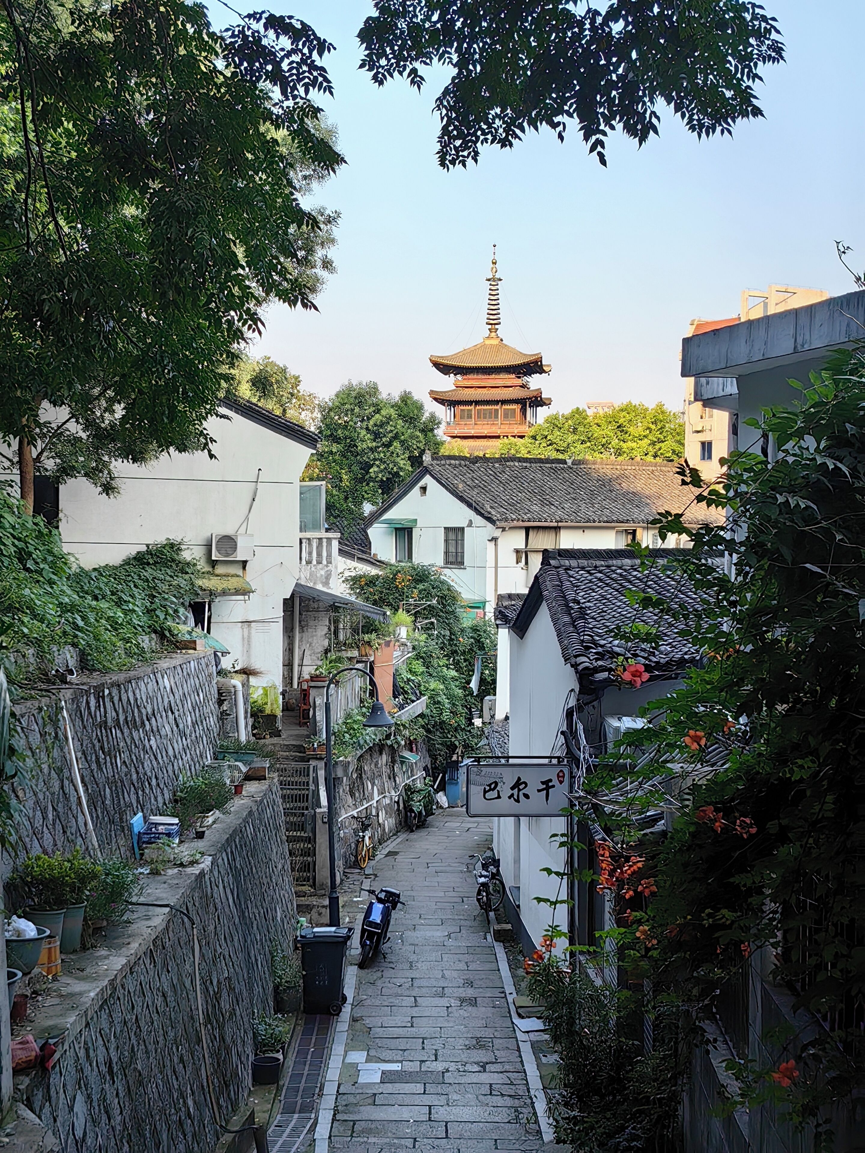 Ein schmaler Gang mit traditioneller Architektur, im Hintergrund eine Pagode und ein Schild mit chinesischen Schriftzeichen.