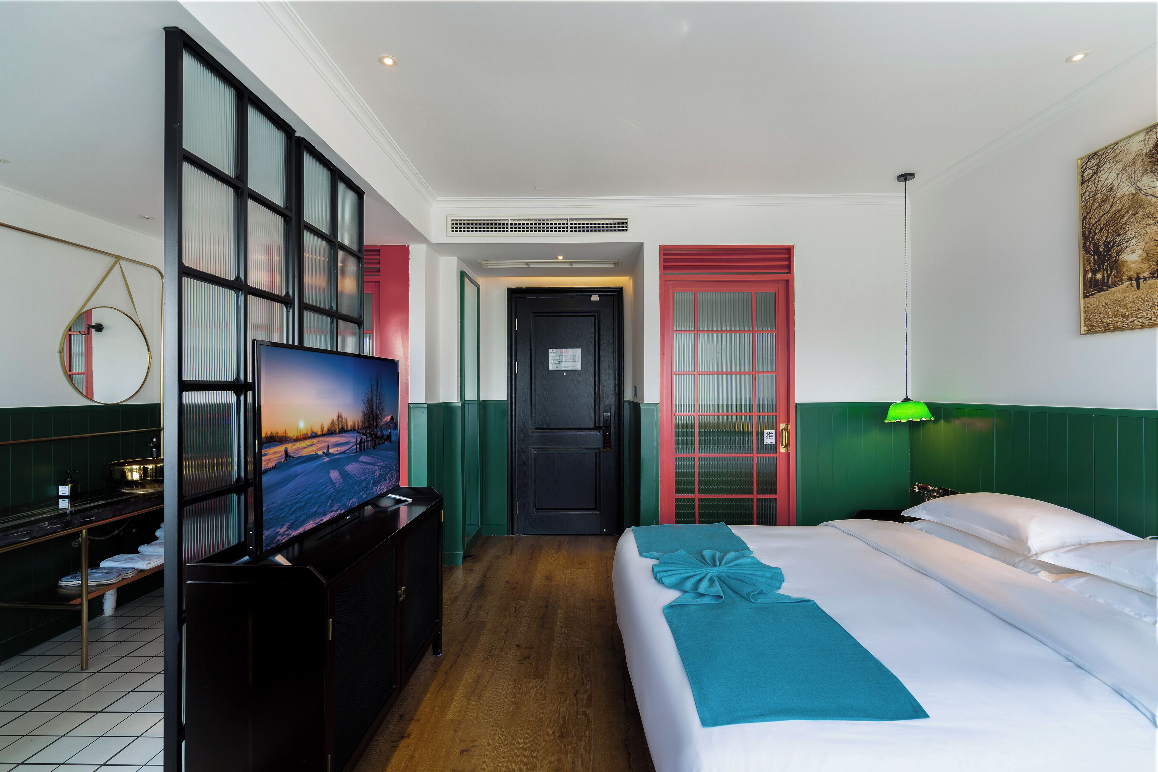 A hotel room with a bed, a television, a desk, and a green wall.