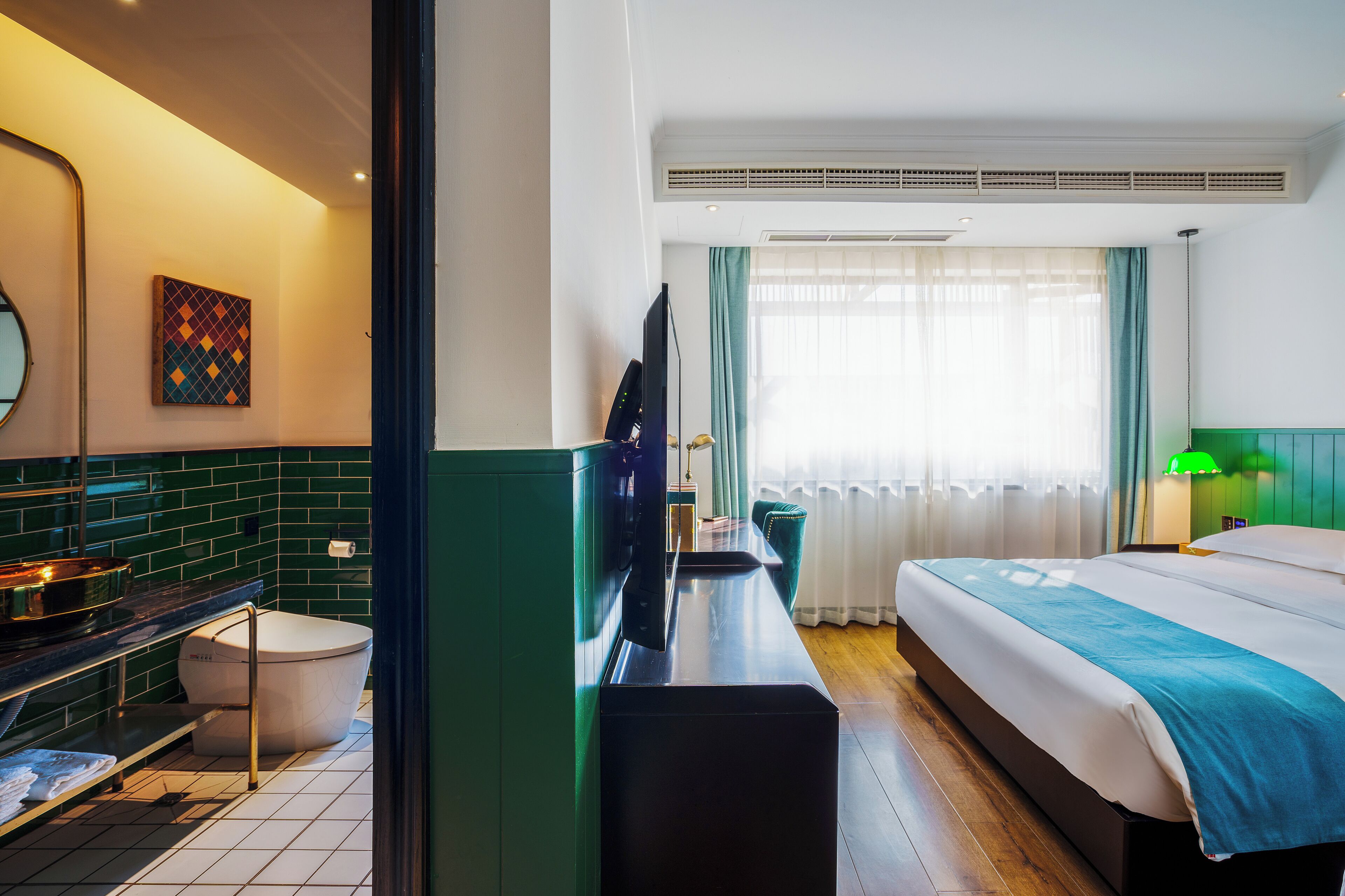 A hotel room with a bed, a desk, a television, a bathroom, and a window with curtains.