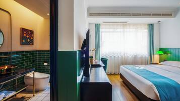 A hotel room with a bed, a desk, a television, a bathroom, and a window with curtains.