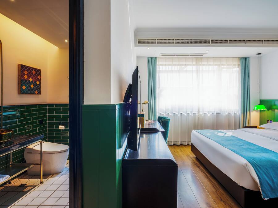 A hotel room with a bed, a desk, a television, a bathroom, and a window with curtains.