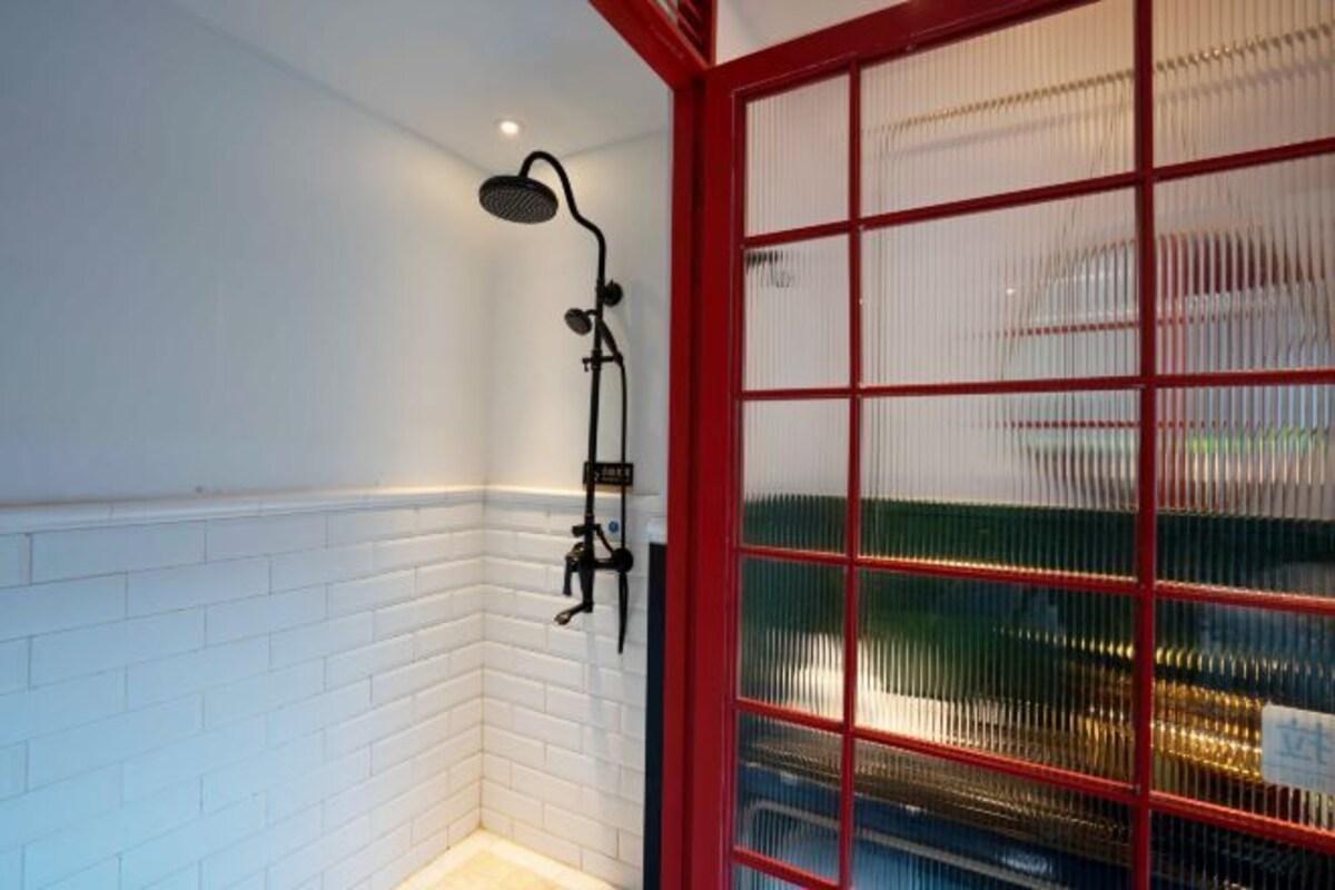A shower area with a white tiled wall, a red-framed glass door, and a black showerhead.