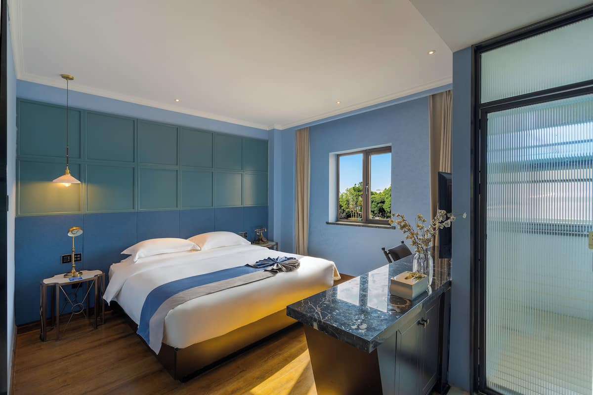 Una habitación de hotel moderna con una cama grande, un escritorio con un florero y una ventana con vistas a zonas verdes.