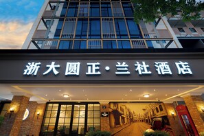 A hotel entrance with a modern facade, a sign with Chinese characters, and a traditional street scene mural. - Zheda Yuanzheng Lanshe Hotel  (Hangzhou)