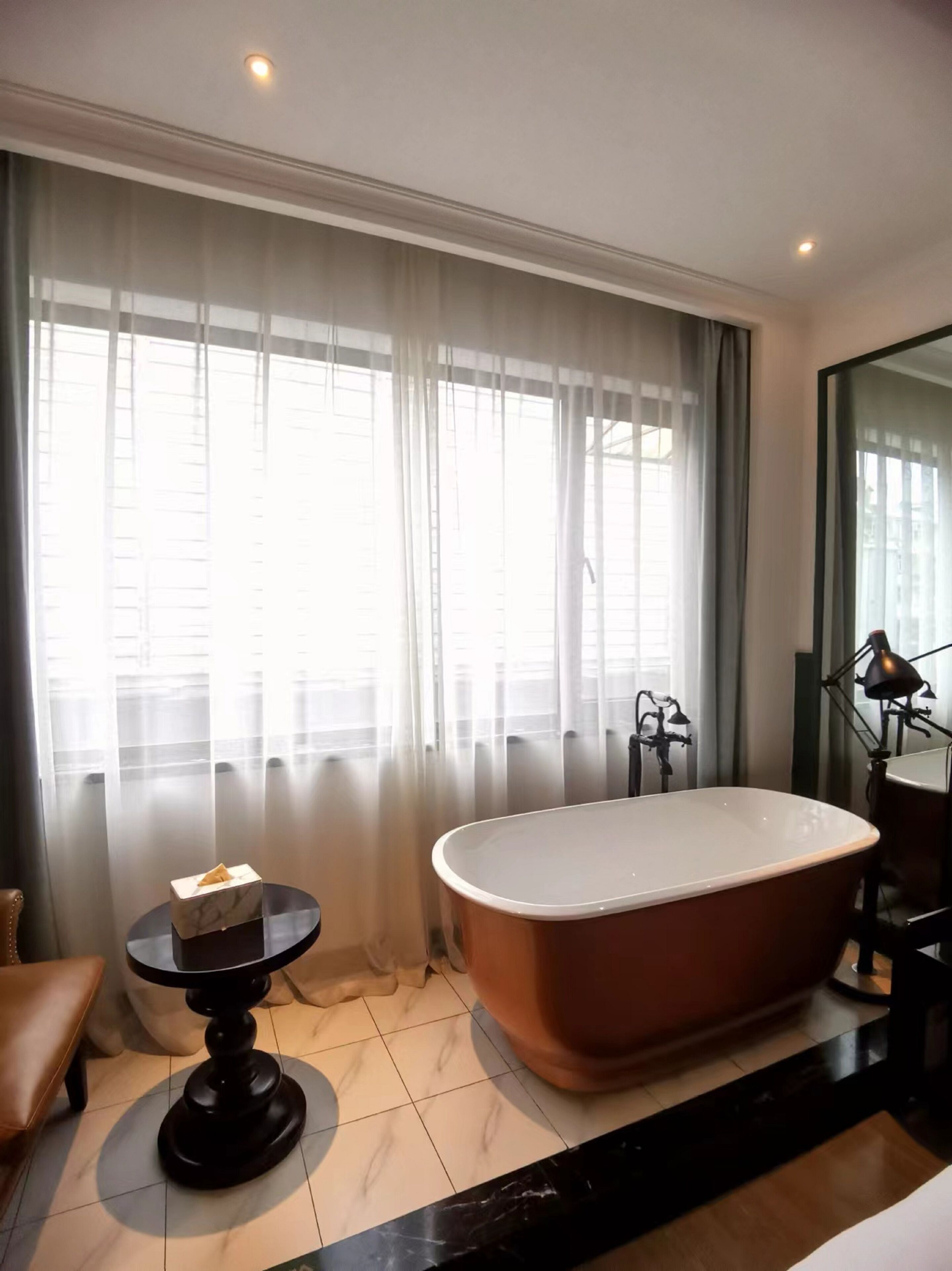 Une salle de bain avec une baignoire sur pieds, une table ronde avec un boîte de mouchoirs et un grand miroir.