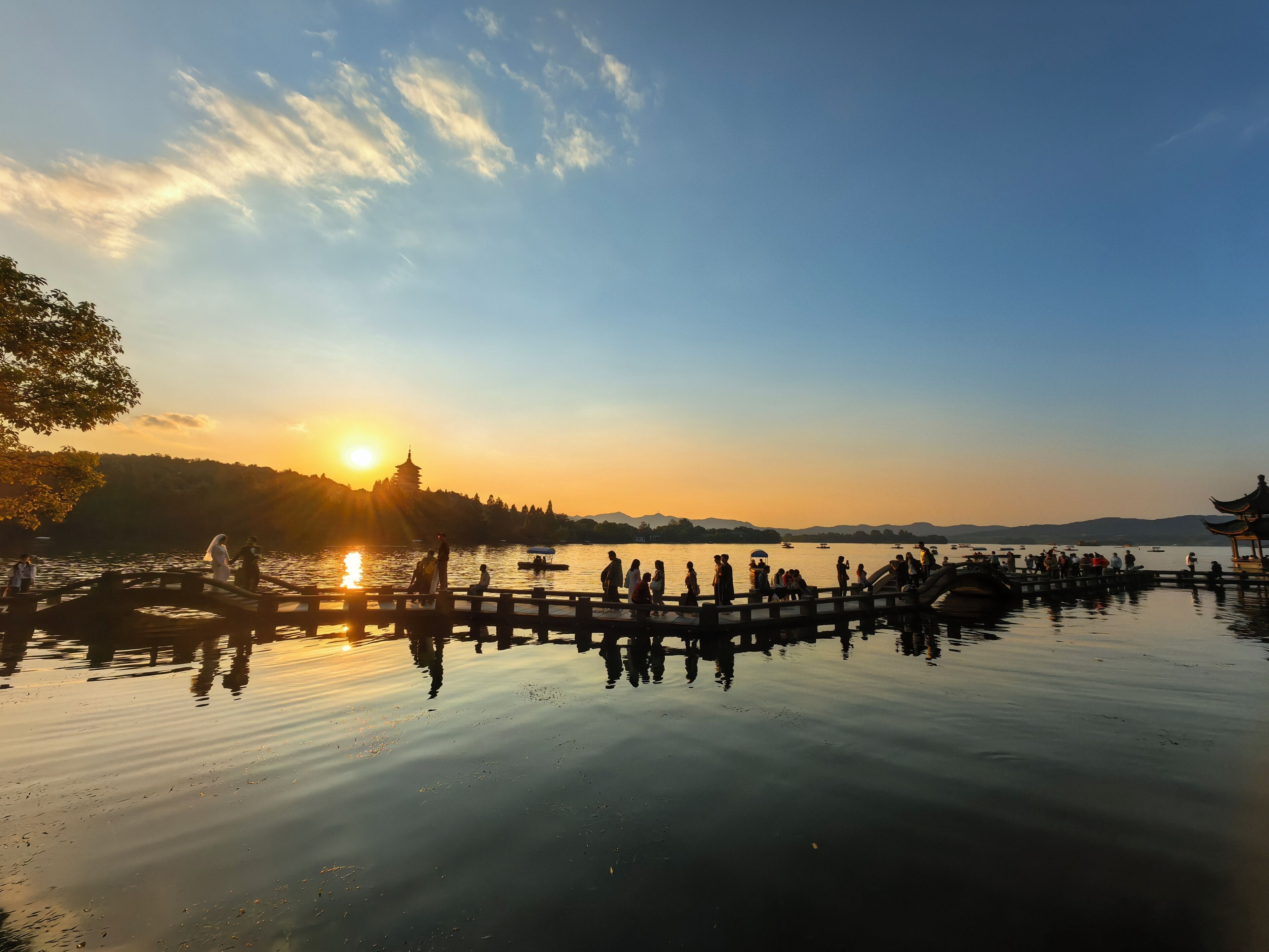 A serene lakeside scene with a wooden bridge, calm water, and a sunset in the background.