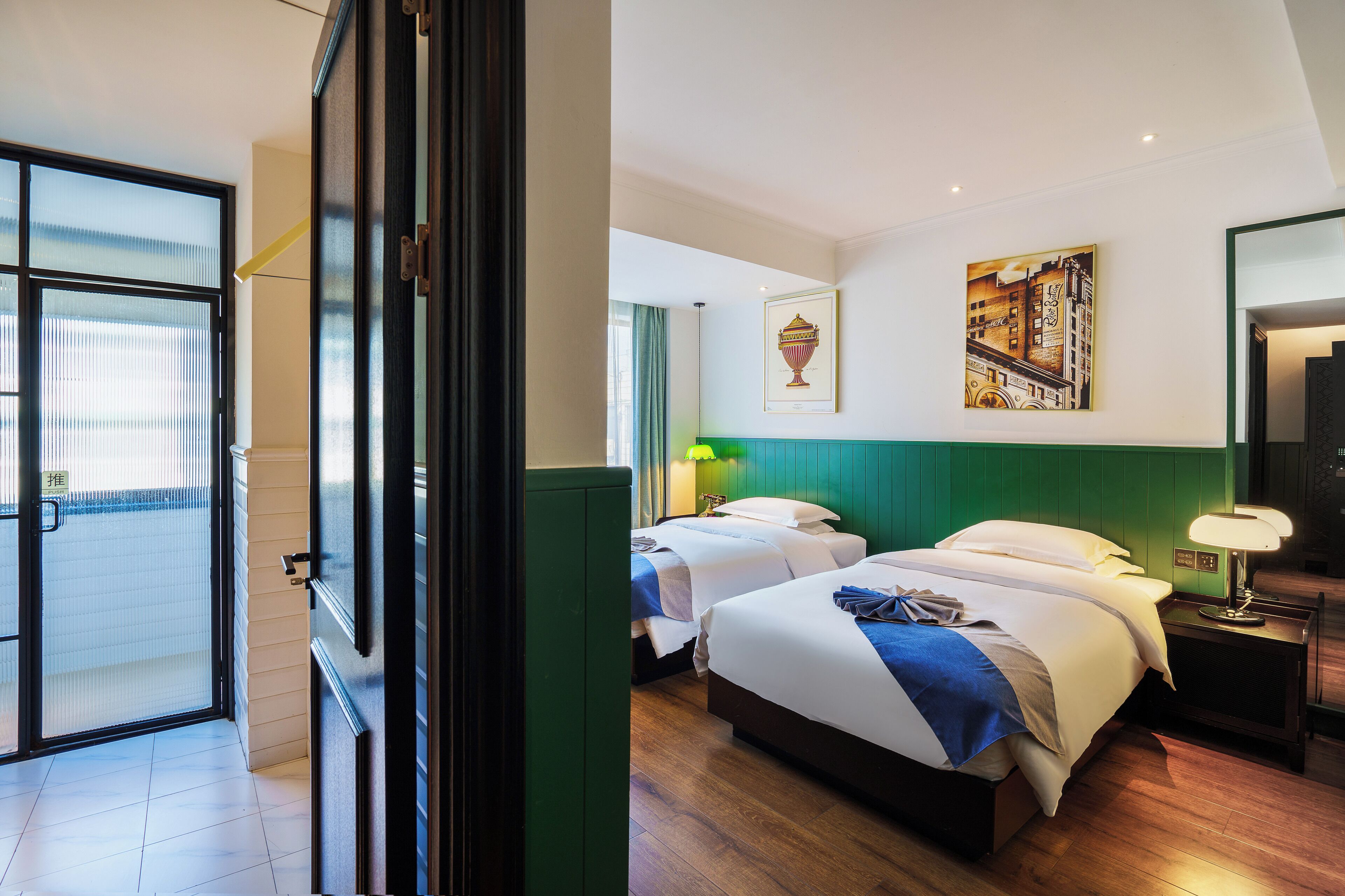 A hotel room with two beds, a green accent wall, and artwork on the wall.