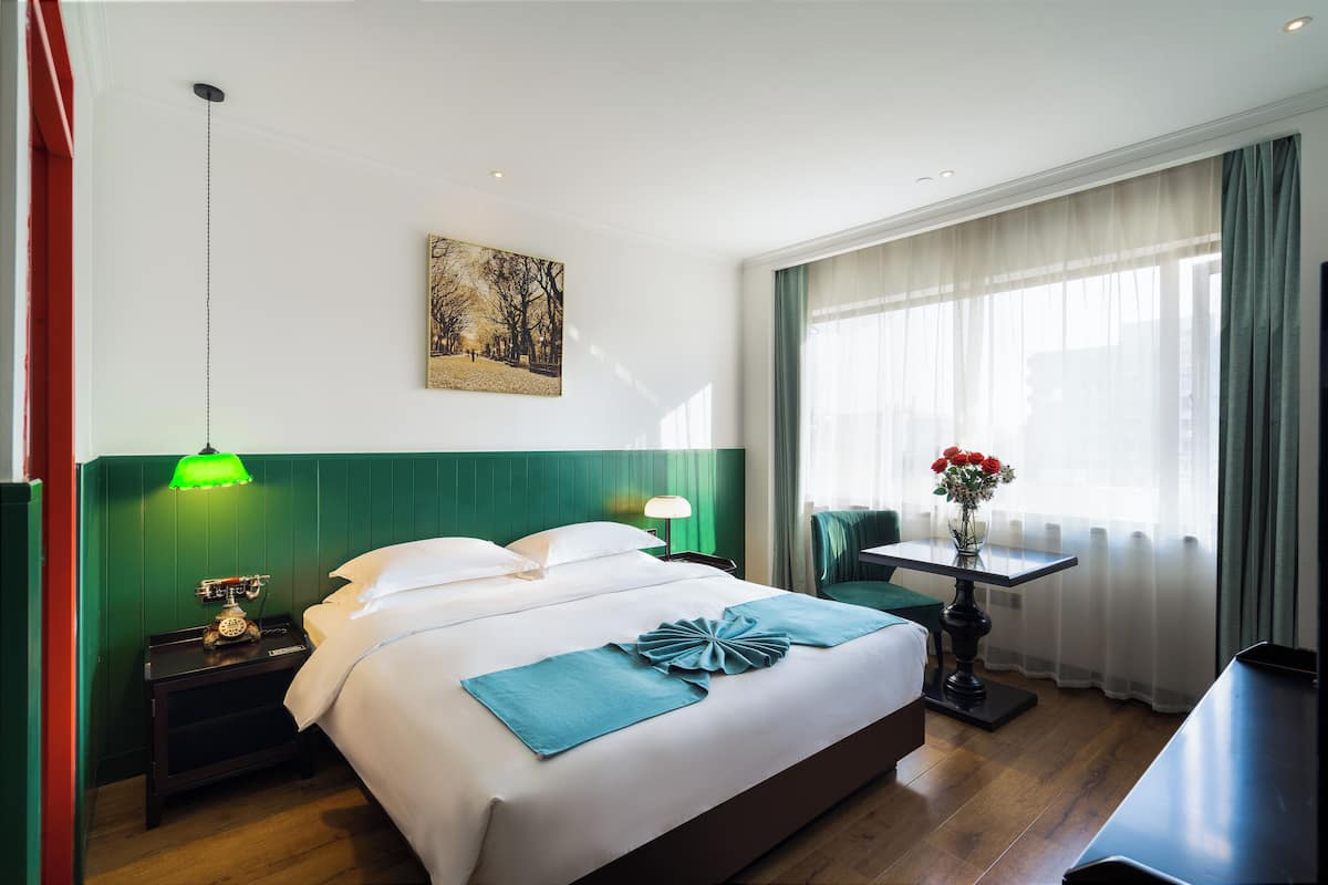 Una habitación de hotel con una cama, una mesita de noche, una mesa con un florero y un cuadro en la pared.