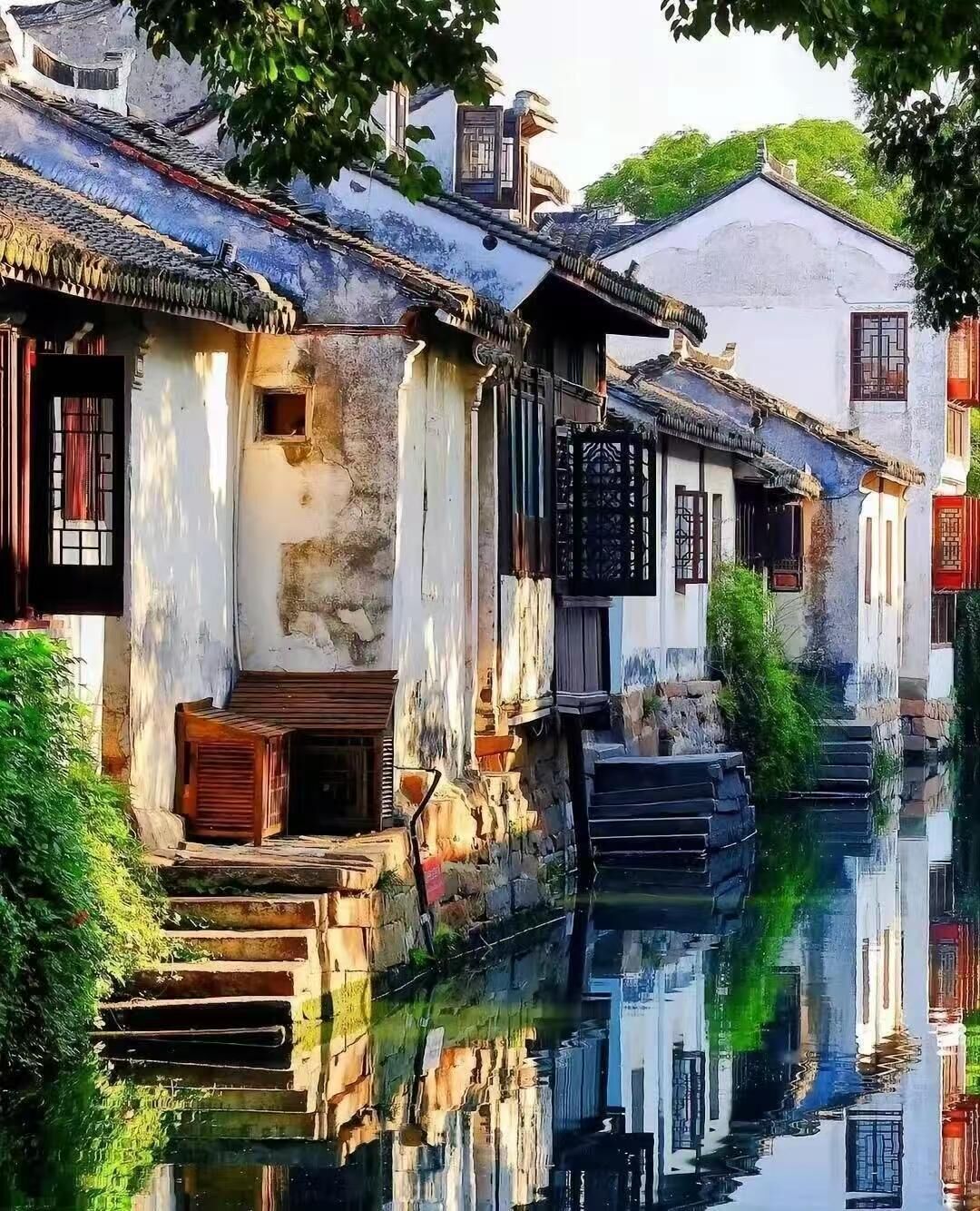 Um edifício tradicional refletido na água, com uma escadaria que leva à entrada e uma pequena janela com uma persiana.