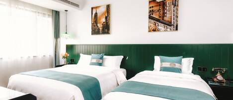 A hotel room with two beds, a green headboard, a window with curtains, and two paintings on the wall.