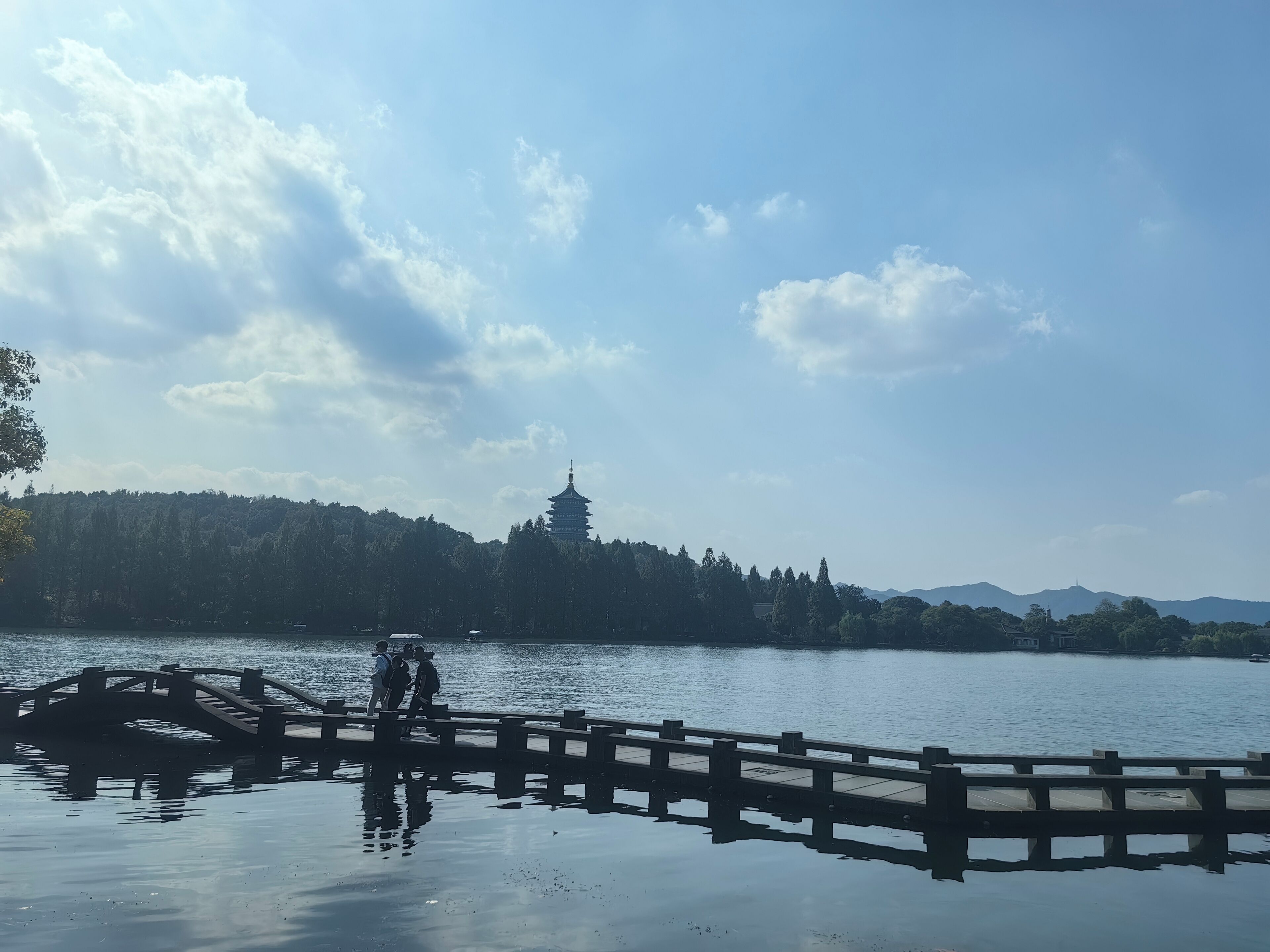 A serene lake with a wooden bridge and a pagoda in the distance.