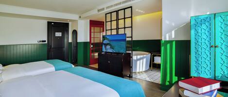 A hotel room with two beds, a TV, a desk with books, a bathtub, and a green and white color scheme.