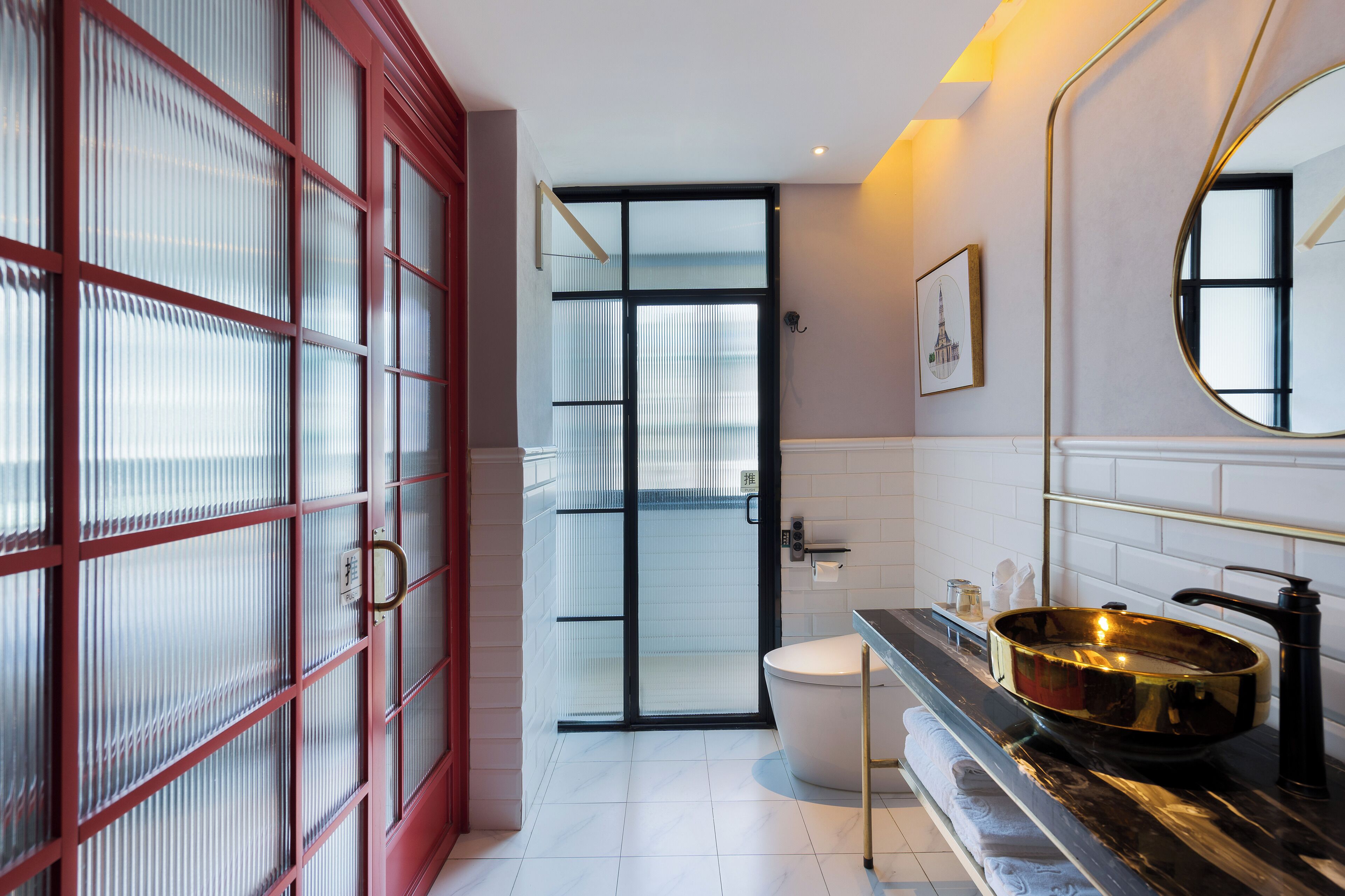 A modern bathroom with a large mirror, a gold sink, and a red-framed glass door.