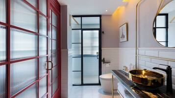 A modern bathroom with a large mirror, a gold sink, and a red-framed glass door.